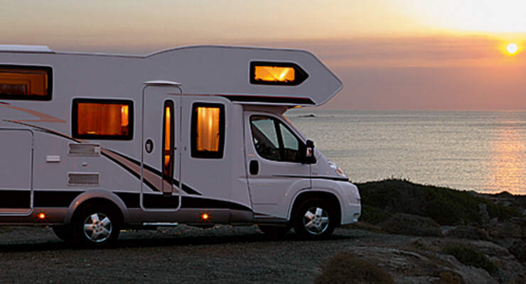 Wohnmobil steht bei Sonnenuntergang am Meer